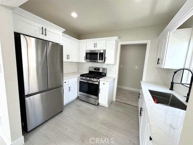 kitchen featuring recessed lighting, a sink, light wood-style floors, appliances with stainless steel finishes, and white cabinetry