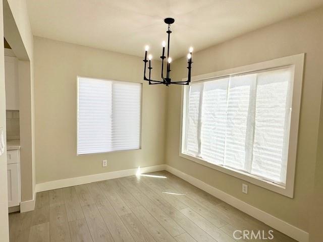 unfurnished dining area featuring baseboards, a notable chandelier, and light wood-type flooring