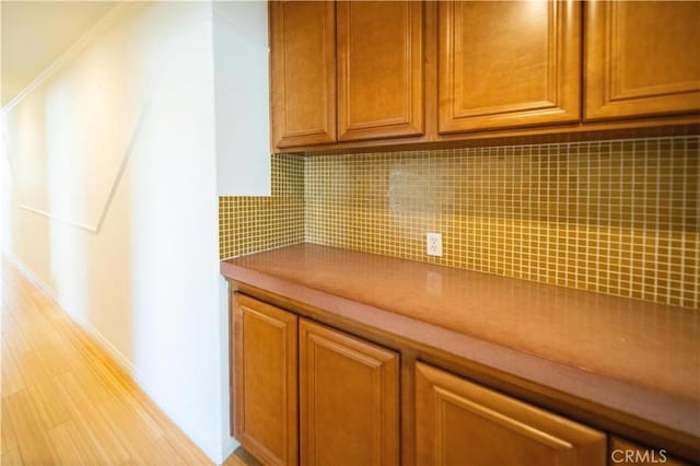 kitchen featuring crown molding, brown cabinets, decorative backsplash, and baseboards