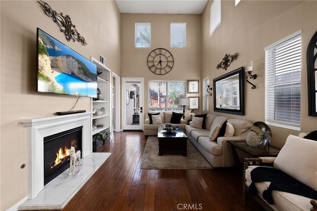 living area featuring plenty of natural light, dark wood-type flooring, a tiled fireplace, and a towering ceiling