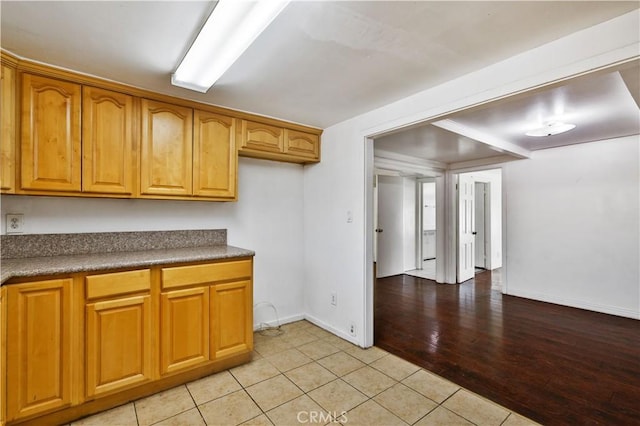 kitchen with brown cabinetry, light tile patterned floors, baseboards, and dark countertops