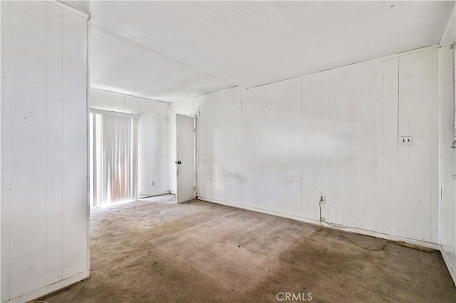 carpeted spare room featuring wooden walls