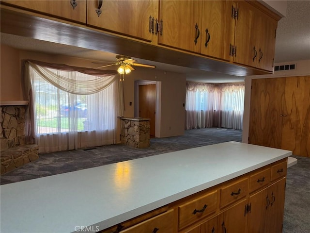 kitchen featuring carpet flooring, a textured ceiling, brown cabinetry, and a ceiling fan