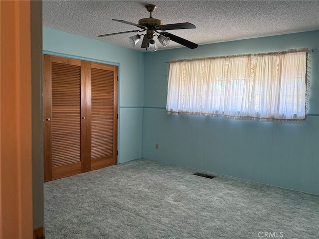 unfurnished bedroom featuring visible vents, a closet, a ceiling fan, a textured ceiling, and carpet floors