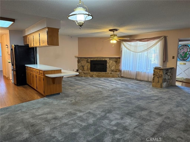 kitchen with a stone fireplace, light countertops, freestanding refrigerator, a ceiling fan, and carpet floors