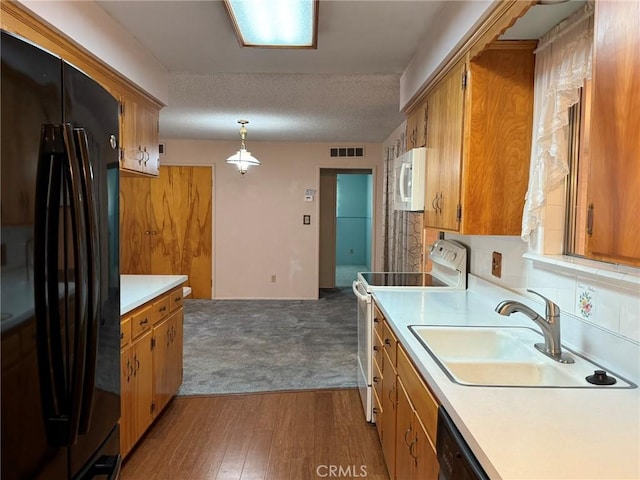 kitchen with a sink, light countertops, brown cabinets, black appliances, and wood finished floors