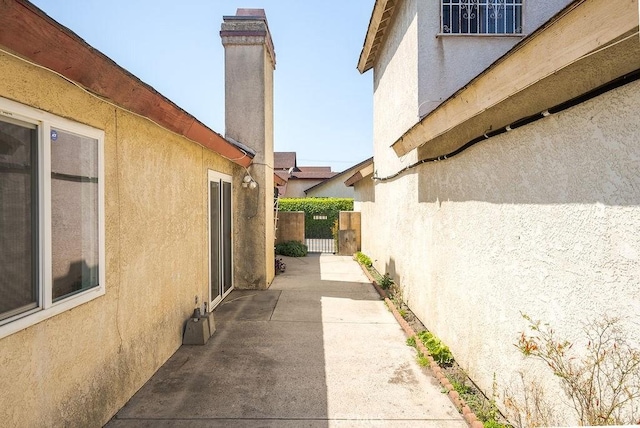 view of property exterior featuring a patio area, stucco siding, a gate, and a chimney