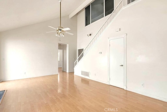 unfurnished living room with ceiling fan, high vaulted ceiling, light wood-style floors, and stairs