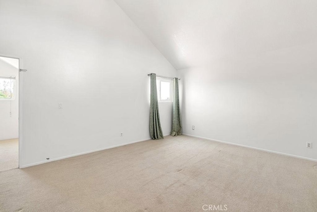 spare room featuring baseboards, high vaulted ceiling, and light carpet