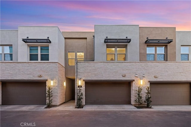 view of property featuring driveway, stucco siding, stone siding, and an attached garage