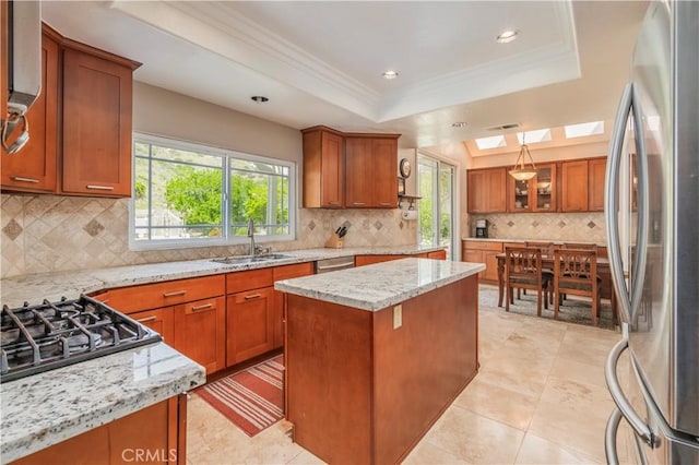 kitchen with brown cabinetry, a tray ceiling, a sink, and appliances with stainless steel finishes