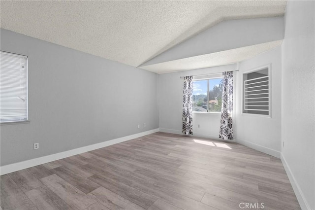 empty room featuring a textured ceiling, vaulted ceiling, and wood finished floors