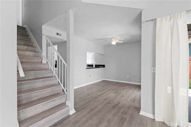 stairway featuring visible vents, baseboards, ceiling fan, a textured ceiling, and wood finished floors