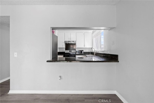 kitchen with baseboards, white cabinets, a sink, a textured ceiling, and under cabinet range hood