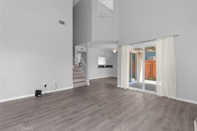 unfurnished living room featuring a towering ceiling, a ceiling fan, stairway, wood finished floors, and baseboards