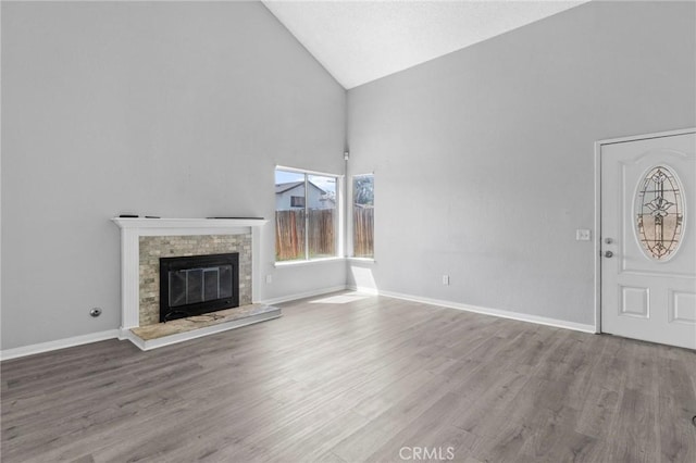 unfurnished living room featuring wood finished floors, high vaulted ceiling, baseboards, and a glass covered fireplace
