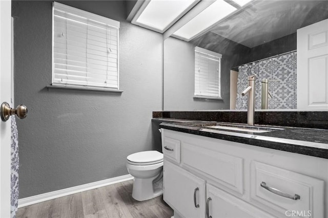 bathroom with toilet, baseboards, vanity, and wood finished floors