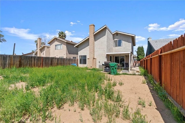 rear view of house featuring a chimney, a fenced backyard, and stucco siding