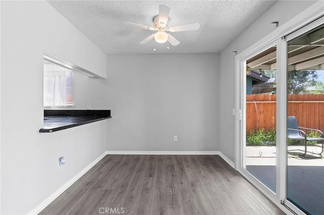 unfurnished dining area with baseboards, a textured ceiling, a ceiling fan, and wood finished floors