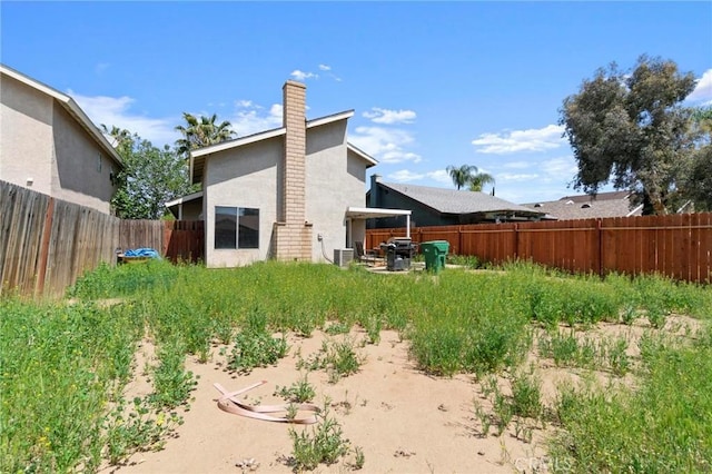 rear view of property featuring a fenced backyard, stucco siding, cooling unit, and a chimney