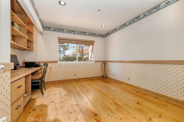 unfurnished office featuring baseboards, light wood-type flooring, wallpapered walls, built in study area, and a wainscoted wall