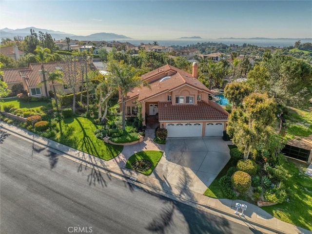 view of front of property featuring a mountain view, a tiled roof, a chimney, concrete driveway, and stucco siding