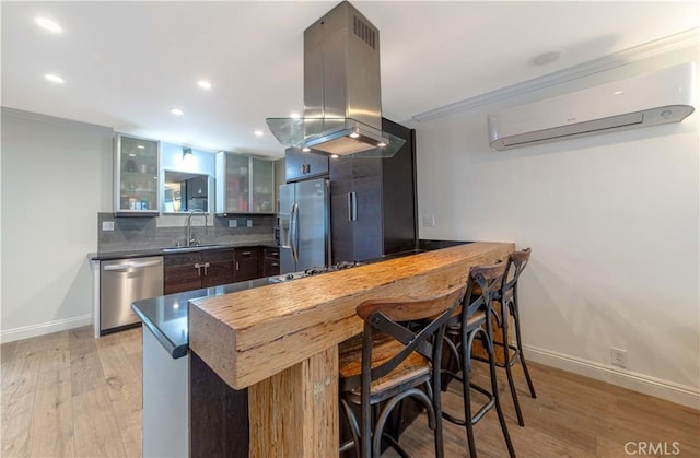 kitchen featuring island exhaust hood, an AC wall unit, ornamental molding, a sink, and appliances with stainless steel finishes