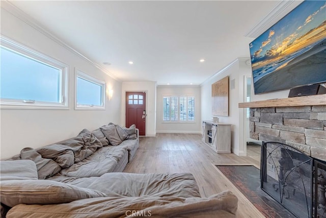 living room with a stone fireplace, crown molding, baseboards, and light wood-style flooring