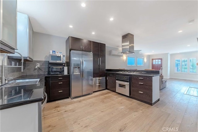 kitchen featuring island range hood, a peninsula, dark brown cabinets, and stainless steel appliances