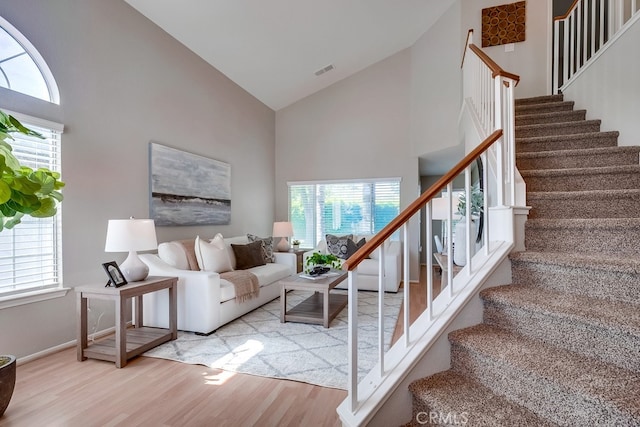 stairway featuring high vaulted ceiling, wood finished floors, plenty of natural light, and baseboards