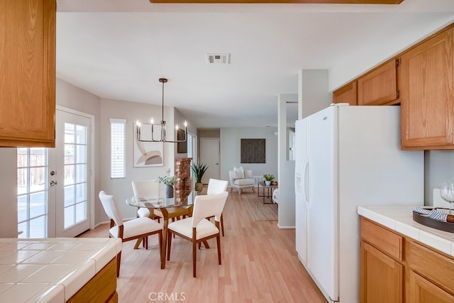 kitchen featuring tile countertops, white fridge with ice dispenser, light wood finished floors, a chandelier, and open floor plan