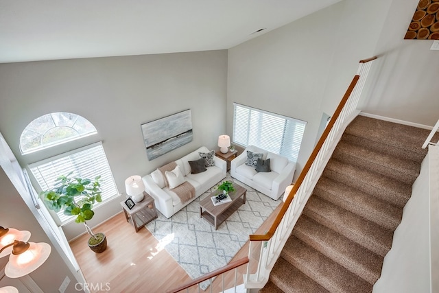 living area featuring stairs, high vaulted ceiling, and baseboards