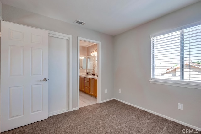 unfurnished bedroom with multiple windows, light carpet, baseboards, and ensuite bath