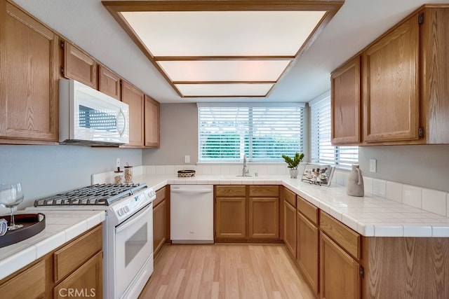 kitchen featuring white appliances, light wood-style flooring, a sink, and tile countertops