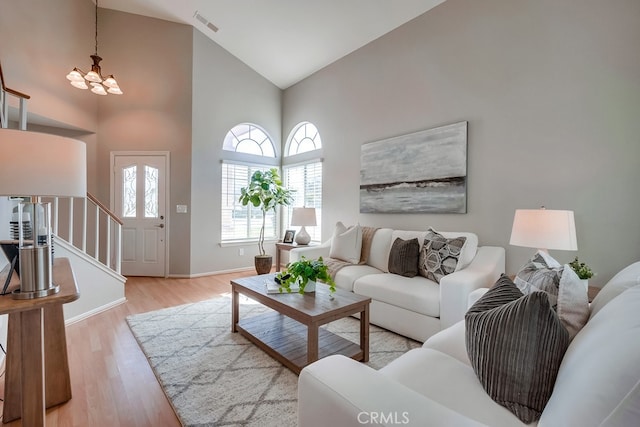 living room with high vaulted ceiling, a chandelier, stairs, light wood finished floors, and baseboards