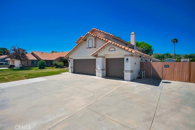 mediterranean / spanish house with stucco siding, concrete driveway, a tile roof, an attached garage, and a chimney