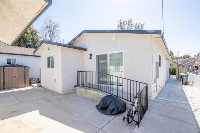 back of property with stucco siding, an outdoor structure, a shed, a patio area, and fence