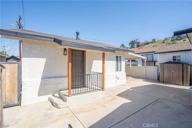 back of property featuring a patio, stucco siding, a shed, an outbuilding, and fence