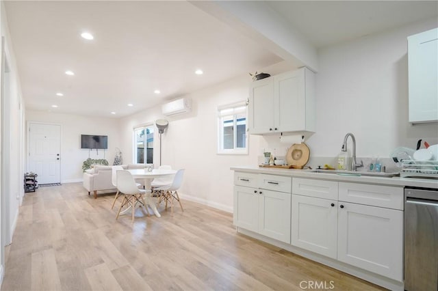 kitchen featuring stainless steel dishwasher, light wood-type flooring, white cabinets, a sink, and a wall mounted air conditioner