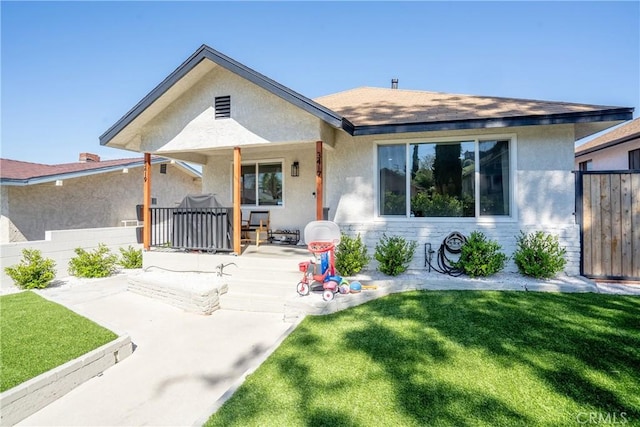 rear view of property featuring covered porch, stucco siding, fence, and a lawn