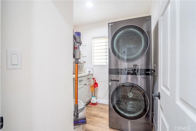 laundry area featuring light wood-style flooring, stacked washer and clothes dryer, laundry area, and baseboards