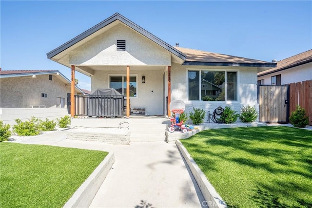 bungalow-style house with stucco siding, fence, a front lawn, and a gate