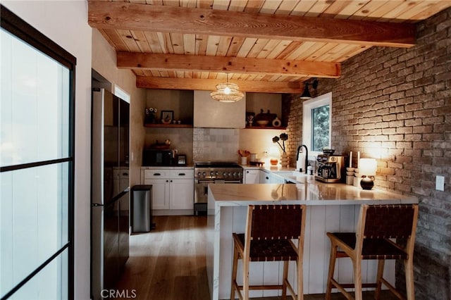kitchen featuring a sink, a peninsula, black appliances, white cabinetry, and wood finished floors