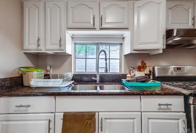 kitchen with a sink, under cabinet range hood, stainless steel range with gas cooktop, dark stone countertops, and white cabinets