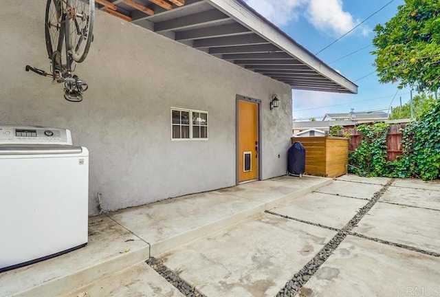 view of property exterior with fence, stucco siding, washer / clothes dryer, and a patio area