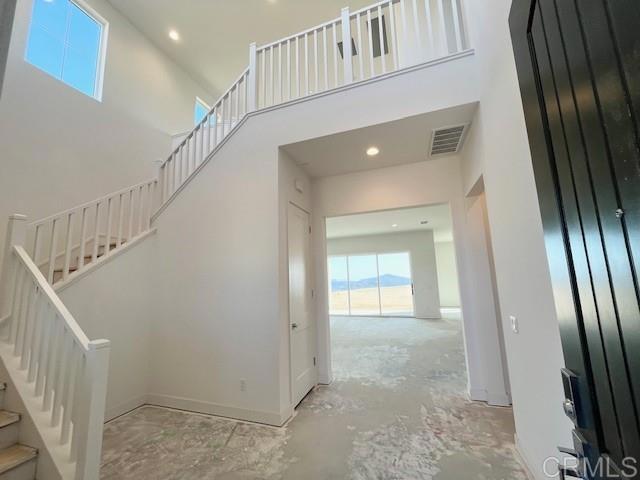 staircase featuring a towering ceiling, baseboards, recessed lighting, visible vents, and concrete flooring
