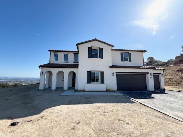 view of front of house with a tiled roof, aphalt driveway, a garage, and stucco siding