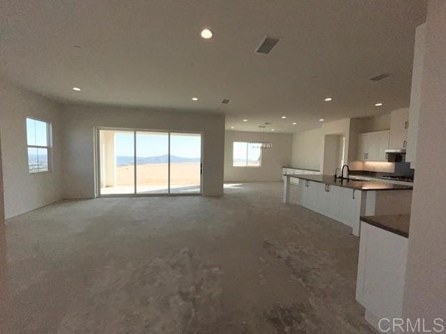 unfurnished living room with a sink, visible vents, recessed lighting, and light carpet