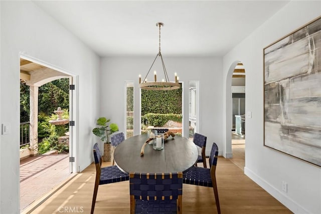 dining area with arched walkways, baseboards, and wood finished floors