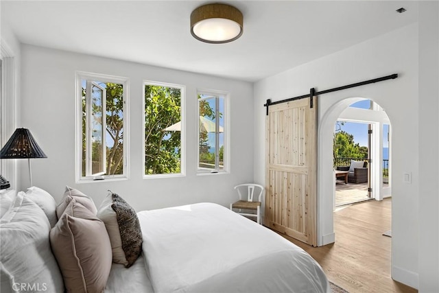 bedroom featuring light wood-type flooring, arched walkways, baseboards, and a barn door